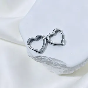 Close-up detail of silver hollow heart-shaped hoop earrings on a white stone base