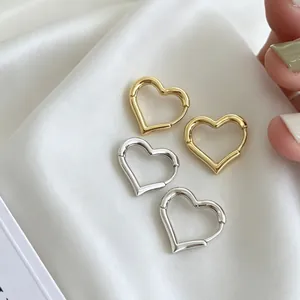 Close-up detail of minimalist gold and silver heart-shaped hoop earrings on white silk fabric