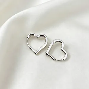 Close-up detail of elegant silver-colored heart-shaped hoop earrings on soft white silk background