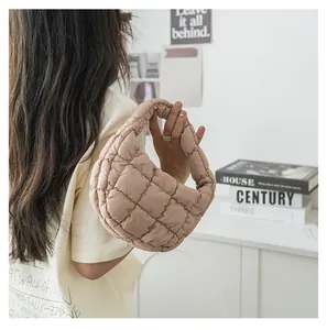 Dettaglio di una mini borsa a nuvola imbottita in beige tenuta da una modella