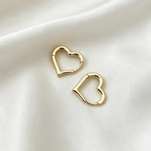 Close-up detail of elegant gold hollow heart hoop earrings placed on white silk fabric
