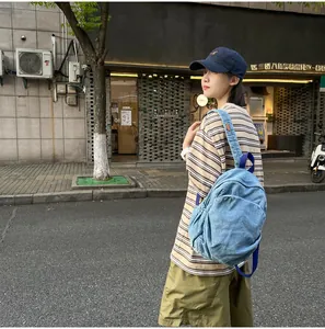 Modelo asiática con mochila de mezclilla lavada retro en un entorno de calle urbana