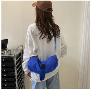 Vista trasera de un bolso bandolera grande de tela oxford azul usado por una modelo en sala.