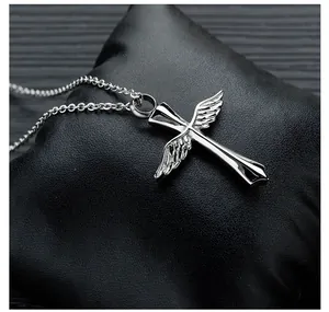 Close-up of a silver winged cross cremation urn pendant on a black textured cushion