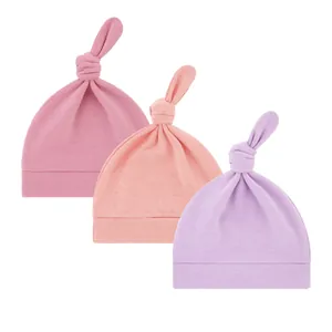 Detailansicht von drei weichen Baumwoll-Babymützen mit Knoten in Rosa, Pfirsich und Lila Tönen.