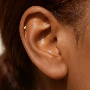Close-up detail of a minimalist gold teardrop stud earring on a cartilage piercing