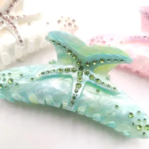 Close-up of starfish hair claw clip with green rhinestones and marble acetate texture.