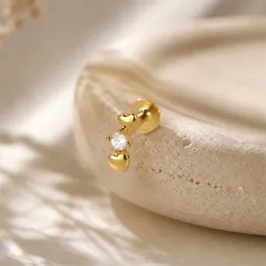 Detailed macro view of a gold-plated heart stud earring with zircon on a stone tray