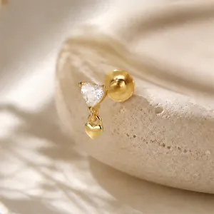 Macro detail of a gold heart-shaped piercing stud with a clear crystal and heart charm