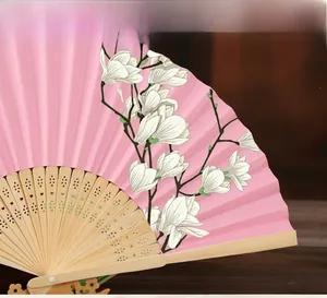 Detail of a pink folding fan with white magnolia pattern and carved bamboo ribs.