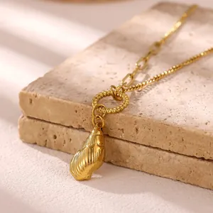 Dettaglio macro di una collana in acciaio inossidabile dorato con pendente a conchiglia.