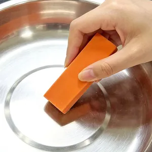 Handheld orange limescale eraser scrubbing a stainless steel pot for deep cleaning