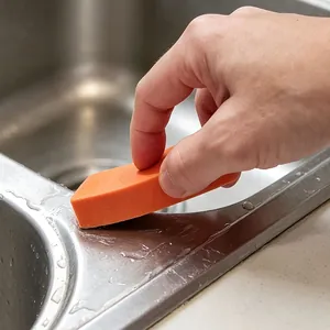 Close-up of an orange cleaning eraser scrubbing a stainless steel kitchen sink surface