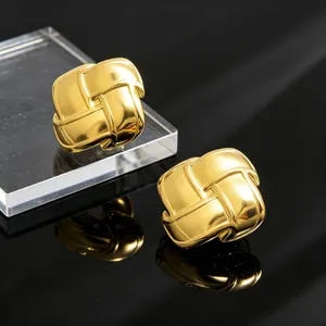 Gros plan de boucles d'oreilles clous géométriques tissées dorées sur surface sombre.