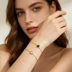 Close-up of elegant double-layer gold bracelets with heart-shaped emerald and diamond gems.