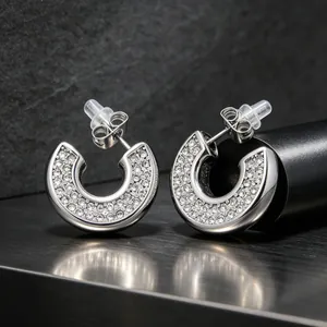 Detailed shot of pavé set crystal C-shaped stainless steel earrings with white gold finish