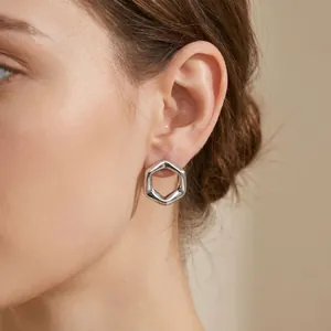 Detailed view of minimalist silver hexagonal hollow stud earrings worn by a model