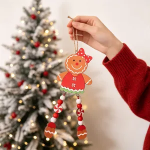 Hand holding a wooden gingerbread man ornament with beaded legs in front of Christmas tree.