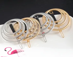 Dettaglio di fermagli geometrici in metallo a tre anelli in oro e argento lucido.
