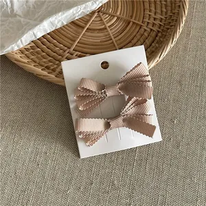 Coppia di eleganti fermagli per capelli con fiocco in gros-grain beige su cartoncino