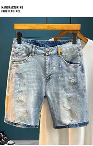 Detail of light blue distressed denim shorts with hand-painted orange and white paint splatters