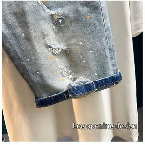 Detail of distressed denim shorts with paint splatters and cuffed hem design.