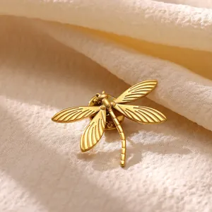 Gros plan d'une broche libellule en or mat avec des ailes gravées détaillées sur tissu