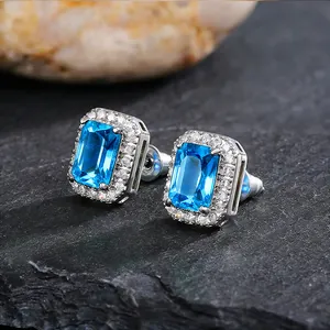 Macro view of silver stud earrings with emerald-cut blue stones and zircon halo.
