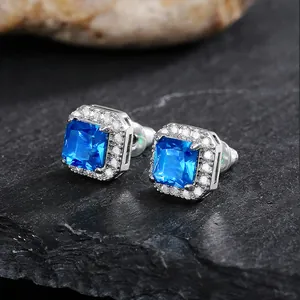 Detailed macro view of square silver stud earrings with vibrant blue center stone and halo