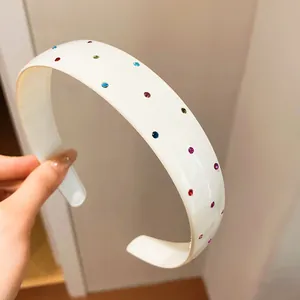 Close-up of a white acrylic wide headband decorated with colorful tiny rhinestones.