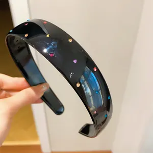 Macro view of colorful sparkling rhinestones set in a wide black acrylic headband.