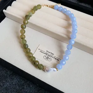 Close-up of green and blue acrylic beads with a central white baroque pearl.