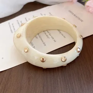 Primo piano di un bracciale in acrilico bianco crema con borchie dorate su legno