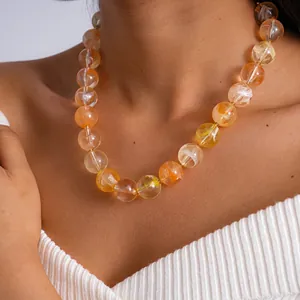 Gros plan d'un collier en acrylique épais avec des perles marbrées oranges sur un mannequin.