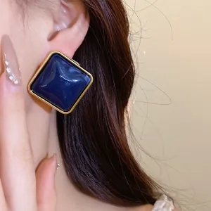 Primo piano di un orecchino quadrato in acrilico blu navy con bordo dorato sull'orecchio