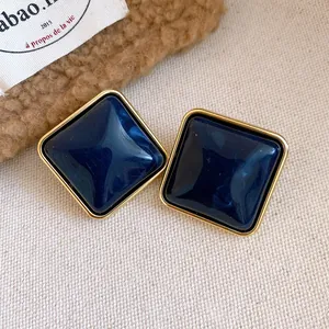 Primo piano di orecchini a lobo quadrati in acrilico blu scuro con bordo dorato