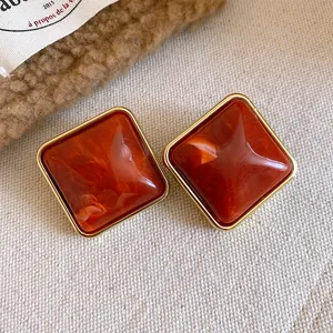 Dettaglio orecchini a lobo a rombo in acrilico marrone-rosso con bordo in metallo oro.