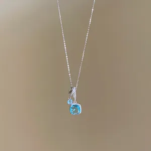Gros plan d'un collier argenté orné d'un pendentif étincelant en zircon bleu carré.