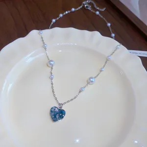 Élégant collier avec cœur en zircon bleu et perles blanches sur une assiette en céramique.