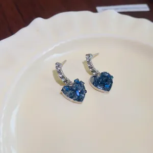 Gros plan de boucles d'oreilles cœur avec cristaux de verre bleus et monture argent.