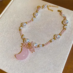 Elegant close-up of a pink crescent moon pendant necklace with pearls and gold accents.