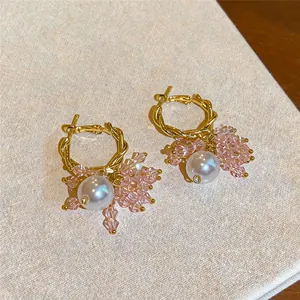 Macro view of gold twisted hoop earrings featuring pink crystal beads and white pearls.