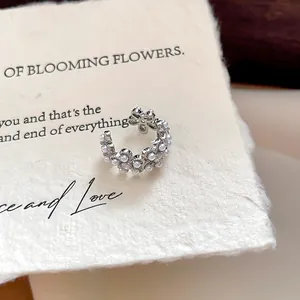 Gros plan d'un ear cuff floral avec perles et zircons sur un papier crème texturé