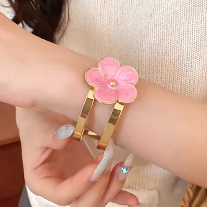 Detalle de un elegante brazalete dorado con flor de esmalte rosa en la muñeca de una modelo