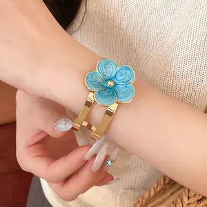 Primer plano de un elegante brazalete dorado con una flor de esmalte azul en la muñeca.