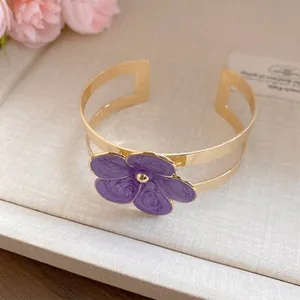 Detalle macro de un elegante brazalete dorado con una flor de esmalte púrpura texturizada