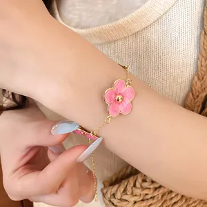 Vista detallada de una elegante pulsera de oro con un colgante de flor de esmalte rosa