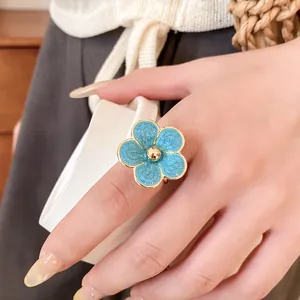 Primer plano de un elegante anillo de flor de esmalte azul usado en un dedo humano