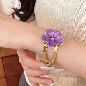 Primer plano de un elegante brazalete dorado con flor de esmalte morado en la muñeca