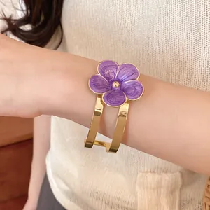 Vista detallada de un elegante brazalete dorado con una flor de esmalte morado en la muñeca.